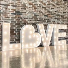 the word love is lit up in front of a brick wall with lights on it