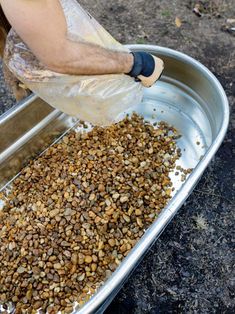 a person scooping food out of a large metal pan into a container on the ground