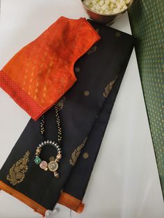 Black Kancheepuram silk saree with orange selvedge. The saree has tiny and large flower gold zari motifs all over the body and the pallu has traditional kattam buttis and Mayil patterns in gold zari. The blouse is black Kanchipuram silk with orange selvedge. This silk saree gives a stunning woven pattern, a masterpiece of artistry and craftsmanship. Draped in this, you will exude timeless charm and sophistication. South Indian Saree, Blouse Tutorial, South Silk Sarees, Designer Sarees Collection, Sari Blouse Designs, Indian Saree Blouse, Indian Fashion Saree, Ethnic Sarees, Indian Saree Blouses Designs