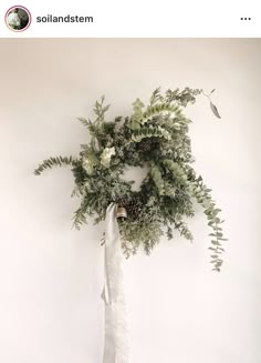 a wreath hanging from the side of a wall with greenery and pine cones on it