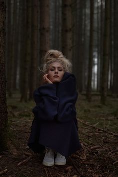 a woman is sitting in the woods with her head on her hands and looking at the camera