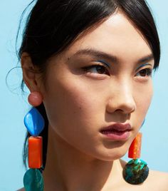 a close up of a person wearing earrings with different colored stones on the ends of them