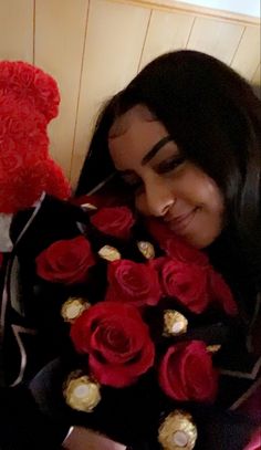 a woman holding a bouquet of red roses and a teddy bear in her lap while smiling at the camera