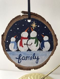 a wooden ornament with three snowmen on it and the word family written in blue