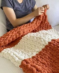 a woman sitting on a couch holding an orange and white crocheted blanket