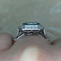 a woman's hand holding an engagement ring with a green stone in the center