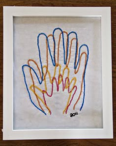 an embroidered handprint in a white frame on a wooden table with a brown background