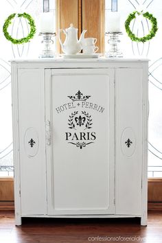 a white cabinet sitting in front of a window with wreaths on the windowsill