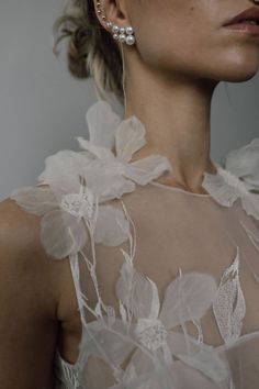 a woman in a white dress with flowers on her neck and earring, looking off to the side