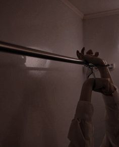 a hand holding onto the handle of a shower curtain in a dark, dimly lit bathroom