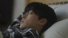 a young man laying in bed with his eyes closed and head resting on the pillow