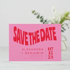 a pink save the date card sitting on top of a table next to a vase with flowers