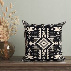 a black and white pillow sitting on top of a wooden table next to a vase