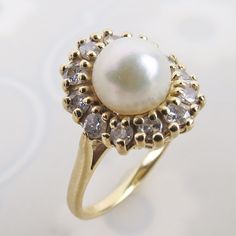 "A lovely natural white pearl tops this elegant 14k yellow gold diamond halo ring. The white lustrous pearl sits 7/16 inch tall above the finger. A row of twelve tiered 2mm .03 carat diamonds flow around the pearl. The dazzling gemstones top a linear wire gallery and smooth sturdy band.  The inside is stamped \"14k\" (gold purity) with no other identifying hallmarks. The ring has an estimated total weight of .36 carat diamonds.  The ring measures an approx. petite size 4.75 and could be re-sized Luxury Formal Pearl Ring With Halo Design, Akoya Pearl Rings With Diamond Accents, Timeless Diamond-white Pearl Ring With Diamond Accents, Classic Pearl Ring With Diamond, Classic Pearl Ring With Diamond Center Stone, Timeless Diamond White Pearl Ring With Diamond Accents, Round Diamond Ring With Akoya Pearl And Diamond Accents, Round Akoya Pearl Diamond Ring With Accents, Elegant Pearl Ring With Diamond Center Stone