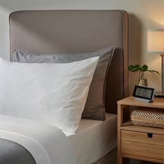 a bed with white sheets and pillows next to a night stand on a wooden nightstand