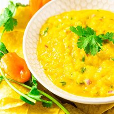 a white bowl filled with yellow salsa surrounded by tortilla chips