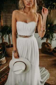 a woman in a white dress and hat posing for the camera with her hand on her hip