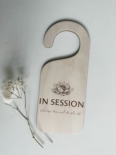 a wooden door hanger with the words in session on it next to some flowers