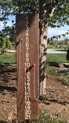 a wooden sign with numbers and chains hanging from it's sides in front of a tree