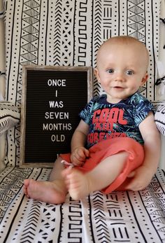 a baby sitting in a chair with a sign that says once i was seven months old