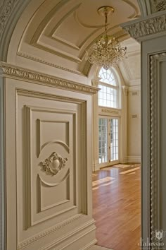 an open door leading to a large room with wood flooring and chandelier