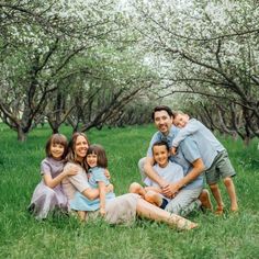 a family poses for a photo in an orchard with blooming trees behind them and grass on the ground