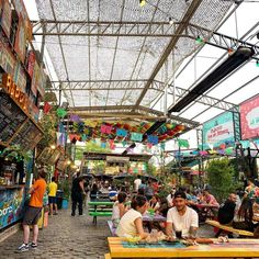 people are sitting at tables in an open air market with lots of signs hanging from the ceiling