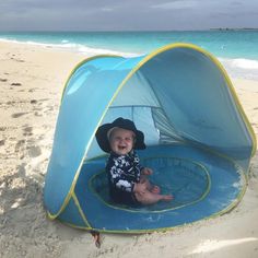 a baby in a blue and yellow tent on the beach