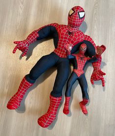 two spider - man action figures are posed on a wood floor, one is holding the other's arm