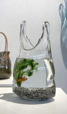 two handbags are on display in front of a glass vase with a fish inside