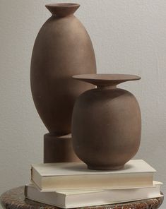 two brown vases sitting on top of a table next to a stack of books