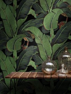 two vases sitting on top of a wooden table in front of a wall with green leaves