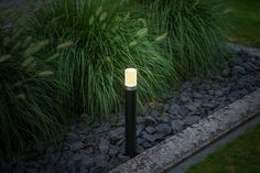 a light that is on in the grass by some rocks and plants with long grass behind it