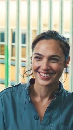 a smiling woman with hoop earrings on her head and blue shirt in front of a fence