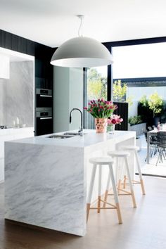 a kitchen with marble counter tops and stools in front of an island that has flowers on it