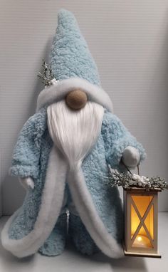 a blue stuffed animal with a white beard next to a lit candle and a small lantern