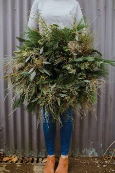 a woman holding a large bush in front of a metal wall and wearing blue pants