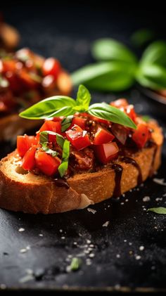 two pieces of bread with tomatoes and basil on top, sitting on a black surface