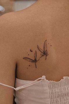 the back of a woman's shoulder with a small dragonfly tattoo on it