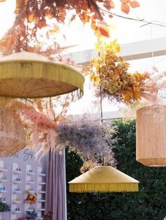 several lamps hanging from the ceiling in an outdoor area with trees and bushes behind them