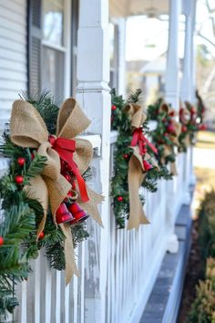 christmas wreaths are hung on the front porch of a house with red and green bows