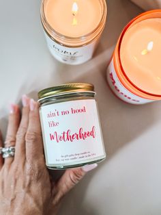 a person holding a candle next to two jars with candles on it and one jar that says, don't no good like motherhood