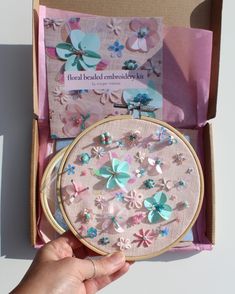 a hand is holding a cross - stitch kit in a box with flowers on it