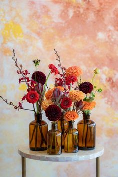 orange and red flowers in brown glass bud vases on a table in front of a warm-colored abstract mural Background Color Palette, Color Palette Autumn, Palette Autumn, Daisy James, Mural Abstract, Dark Red Maroon, Brown Glass Bottles, Rose Dark, Sponge Painting