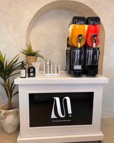 a white counter topped with lots of juice and condiments next to a potted plant