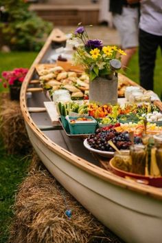 a long boat filled with lots of food on top of a grass covered field next to people