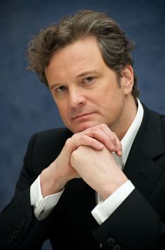 a man in a black suit and white shirt with his hand on his chin looking at the camera