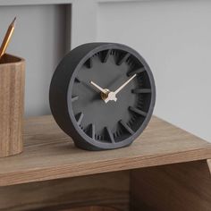 a clock sitting on top of a wooden desk next to a pen and pencil holder