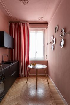 a small kitchen with pink walls and wood flooring in the corner, along with a dining table