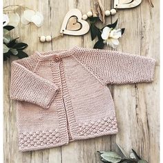 a pink knitted cardigan sitting on top of a wooden floor next to flowers